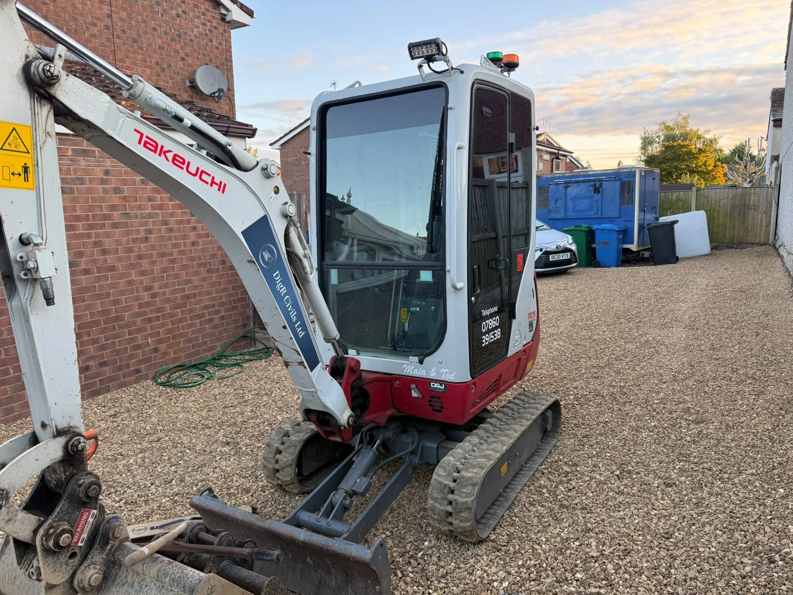 Branded mini digger working beside a house